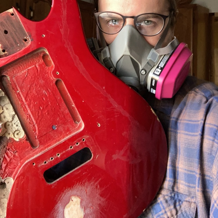 Me in a gas mask holding up the body of my disassembled, badly scratched up guitar